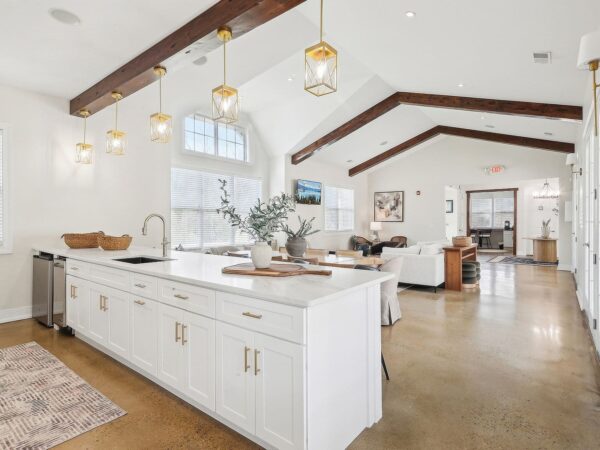Open-concept clubhouse with a large white kitchen island, gold pendant lights, exposed wooden ceiling beams, and a comfortable seating area.